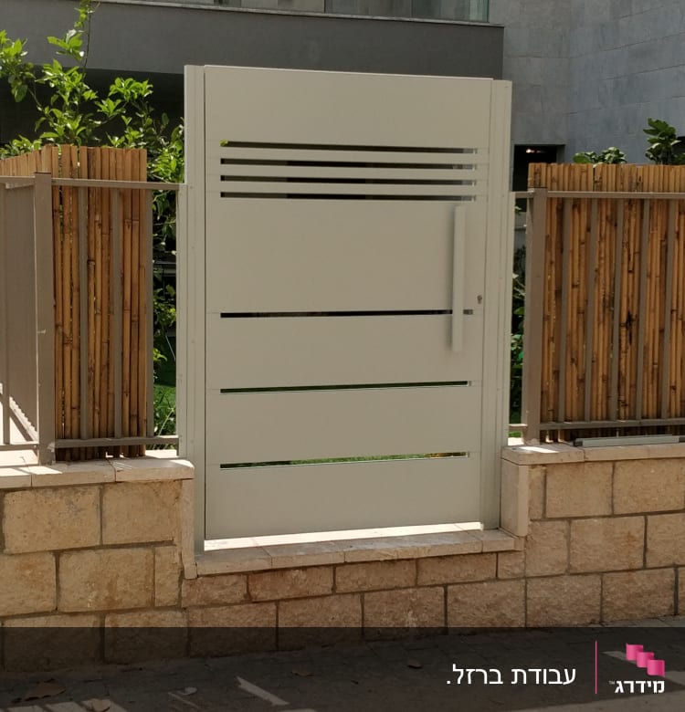 שער מתכת לבן עם פסים אופקיים, מוקף בגדר במבוק.